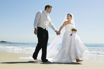 Full length of newlywed couple holding hands while walking on beach
