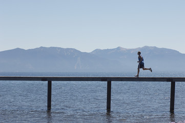 Fototapeta na wymiar Side view of a man running along pier over sea with mountains in the background