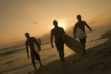 Full length of three surfers carrying surfboards out of surf at sunset