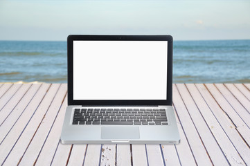 blank screen of laptop on wooden table facing sea with copy spac