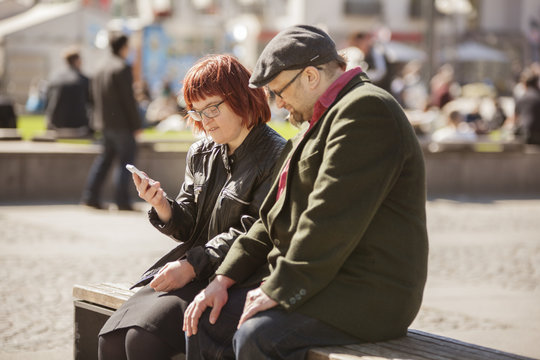 Sweden, Sodermanland, Woman with down syndrome sitting on bench and checking smart phone together with boyfriend