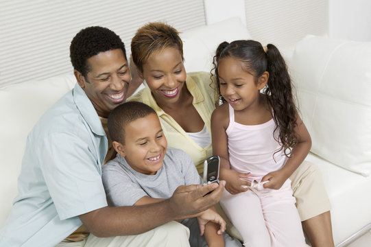 African American family sitting on sofa and looking at picture on camera phone at home