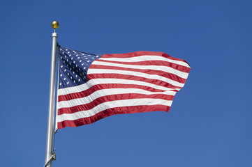 American flag waving on flagpole against blue sky in warm afternoon
