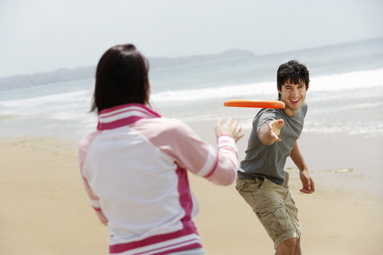Happy couple playing Frisbee on beach during vacation