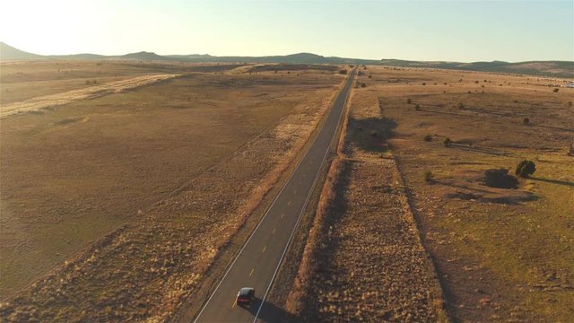 AERIAL: Flying above car driving along empty countryside road at sunset