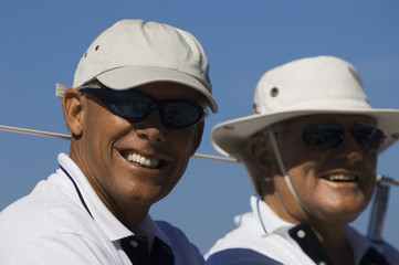 Closeup portrait of two smiling men in sunhats on yacht against clear blue sky