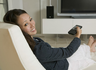 Fototapeta premium Full length portrait of beautiful woman holding remote control while sitting on chair