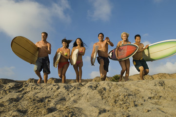 Group of multiethnic friends with surfboards running on sandy beach - Powered by Adobe