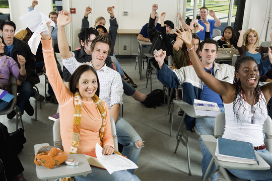 Excited male and female students raising hands in the classroom