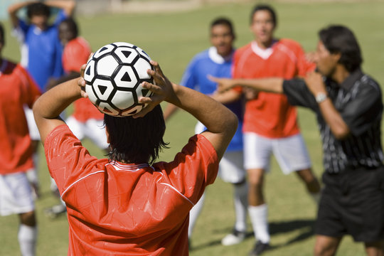 Player ready to throw football while referee whistling and teammates waiting for his instructions