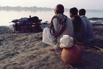 Three figures perform cremation on bank of the River Ganges, Varanasi (Benares)