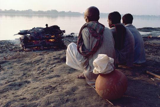 Three figures perform cremation on bank of the River Ganges, Varanasi (Benares)