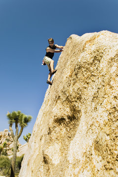 Low angle view of a young man free climbing on cliff against the clear sky
