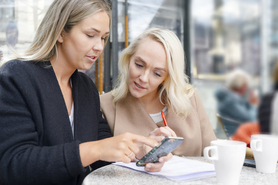 Sweden, Young women using mobile phone at outdoor cafe