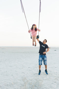 Germany, Schleswig-Holstein, Kreis Nordfriesland, Sankt Peter-Ording, Father pushing daughter (10-11) on swing at beach