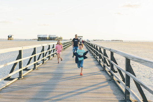 Germany, Schleswig-Holstein, Kreis Nordfriesland, Sankt Peter-Ording, Father with daughter (10-11) and son (8-9) running along boardwalk