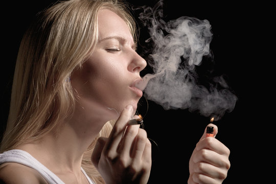 blond young woman smoking on black background
