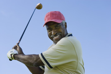 Portrait of a happy senior man swinging a golf club against clear sky
