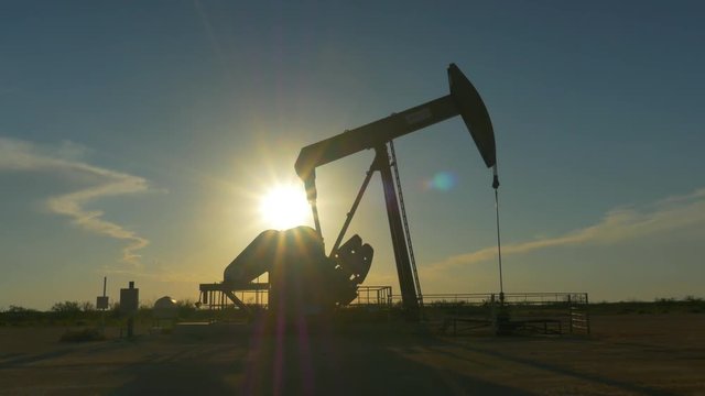 Industrial jack pump platform pumping crude oil over sunset sun