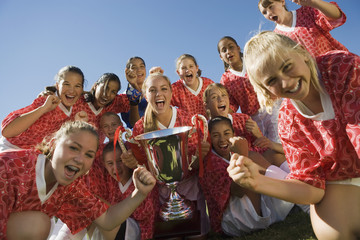 Portrait of excited girls' soccer team holding trophy against clear sky