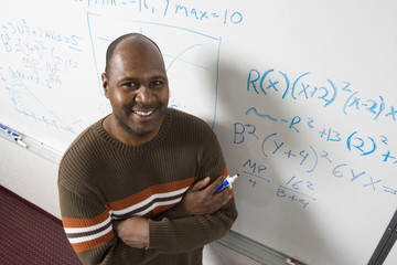 High angle portrait of confident teacher solving math's equations on whiteboard in classroom