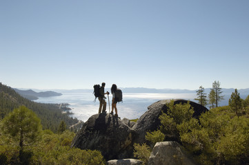 Full length of young hiking couple standing on rock at coast