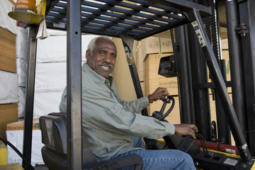 Fototapeta na wymiar Portrait of a happy senior warehouse worker driving forklift