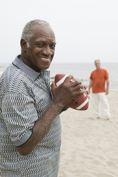Two senior men playing american football on beach