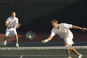 Mixed doubles player hitting tennis ball with partner in the background