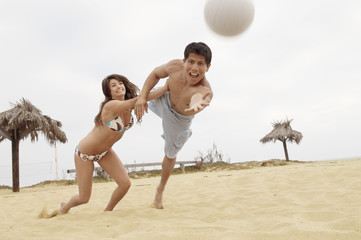 Young woman holding man back from diving for volleyball on the beach