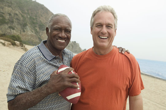 Two men with American football on beach (portrait)