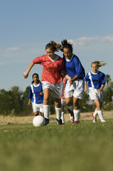 Teenage girls playing soccer on field against the sky