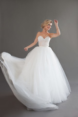 Naklejka premium Dancing young bride in luxurious wedding dress. Pretty girl in white. Emotions of happiness, laughter and smile, gray background