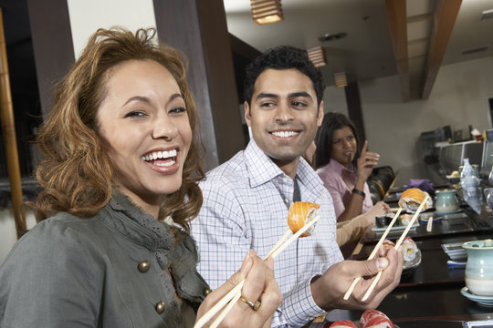Closeup of a smiling woman and friends eating sushi with chopsticks in a restaurant