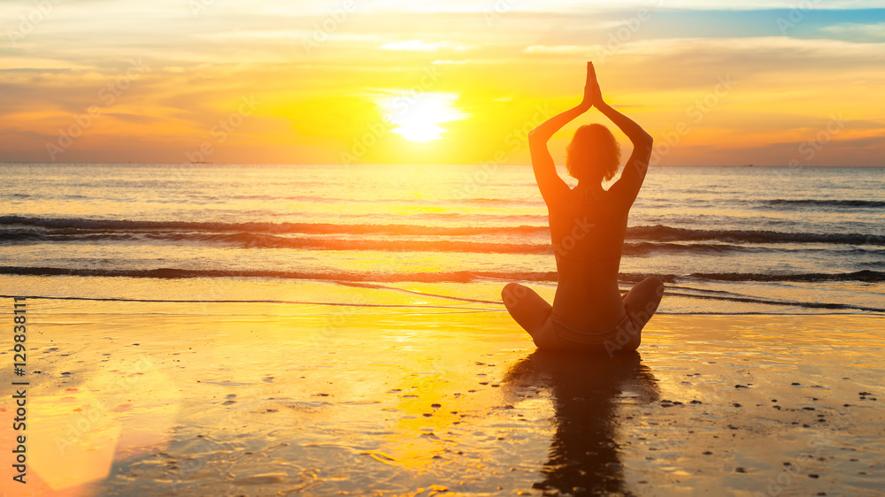 Wall mural Silhouette woman yoga on the sea beach at sunset.