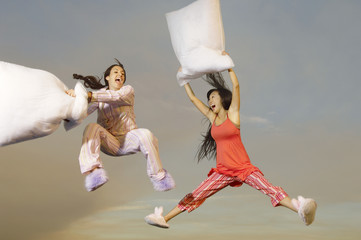 Two multiethnic young women having pillow fight midair outdoors