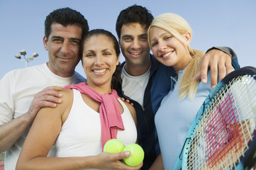Portrait of happy tennis players with rackets and balls against sky