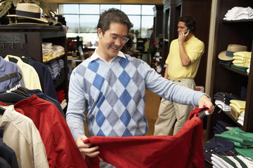 Fototapeta premium Happy mature man selecting shirt with person in background at clothing store