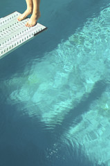 Closeup low section of a female diver standing backwards at the end of diving board over swimming...