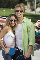 Portrait of young couple standing together while holding tennis bats