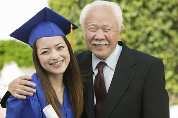 Portrait of happy female graduate and grandfather standing outdoors