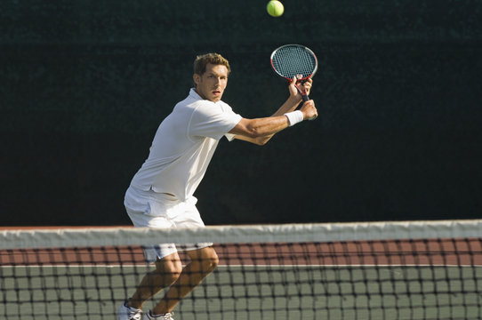 Male tennis player hitting backhand by net on the tennis court