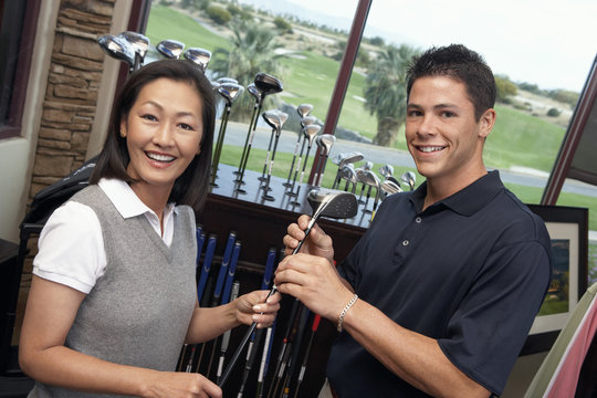 Portrait of happy woman with man selecting golf club in store