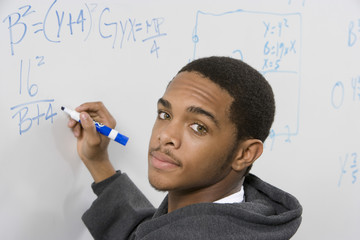 Closeup portrait of male student solving algebra equation on whiteboard in classroom