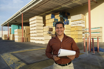Portrait of happy middle aged man with clipboard standing in front of timber factory