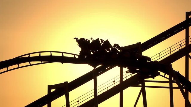 SLOW MOTION: Sunset sun shining through extreme roller coaster ride