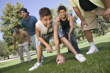 Portrait of a young boy playing American football with group of men in the park