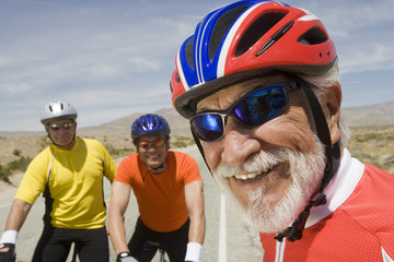 Close-up of a happy senior man with friends riding bicycles in the background