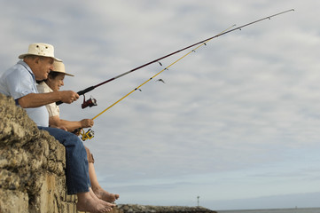 Side view of happy senior couple fishing against cloudy sky