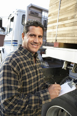 Portrait of a smiling male supervisor with clipboard by truck loaded with wood